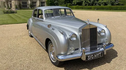 Front side view of silver Rolls-Royce Silver Cloud parked on gravel in Cambridge countryside.