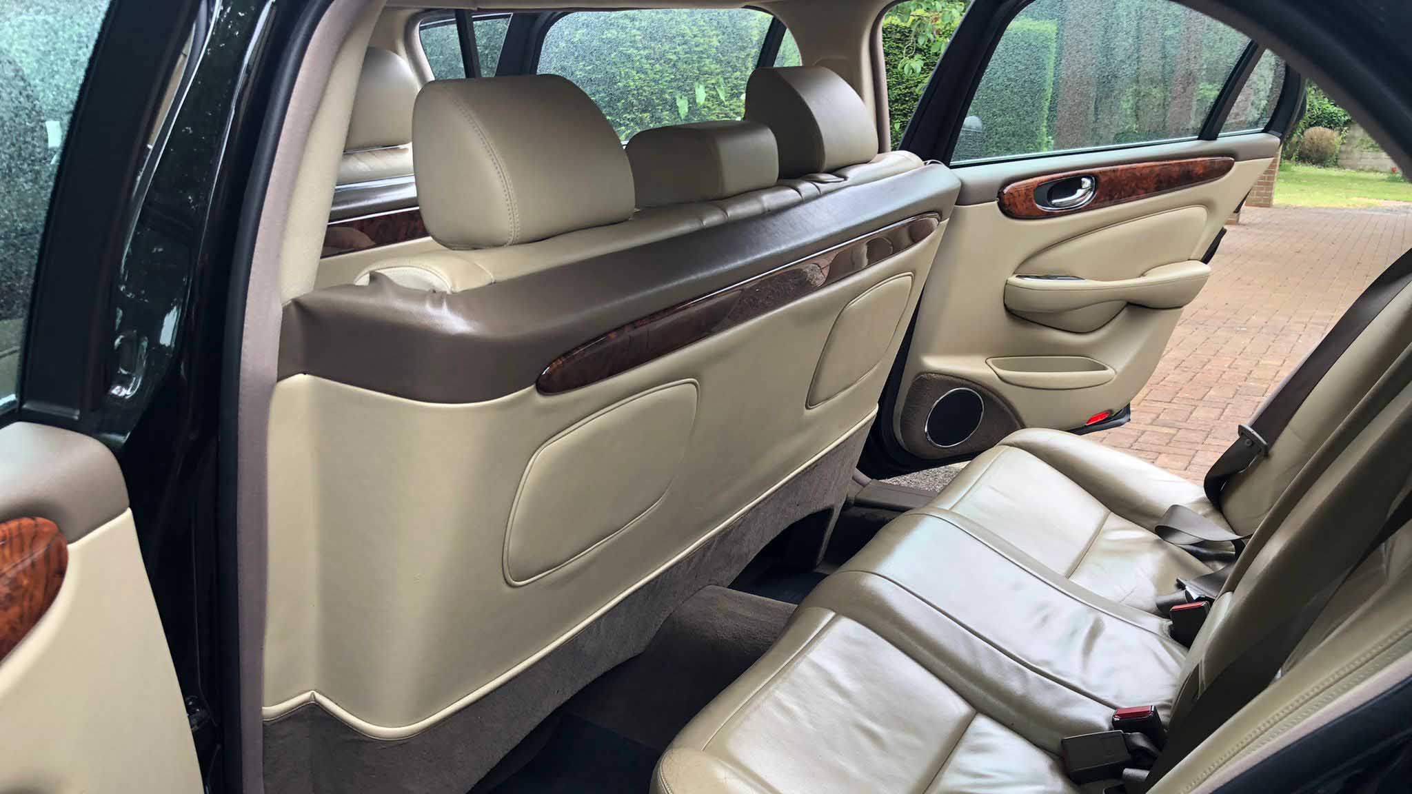 Cream leather rear passenger seating inside black Jaguar stretch limousine with wood trim.