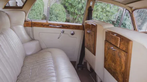 Cream leather rear seating inside classic 1960 Rolls-Royce Silver Cloud with polished wood trim.