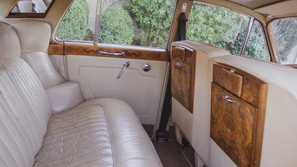 Cream leather rear seating inside classic 1960 Rolls-Royce Silver Cloud with polished wood trim.