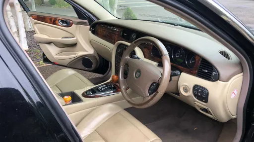 Driver’s seat and dashboard inside black Jaguar stretch limousine with cream leather interior.