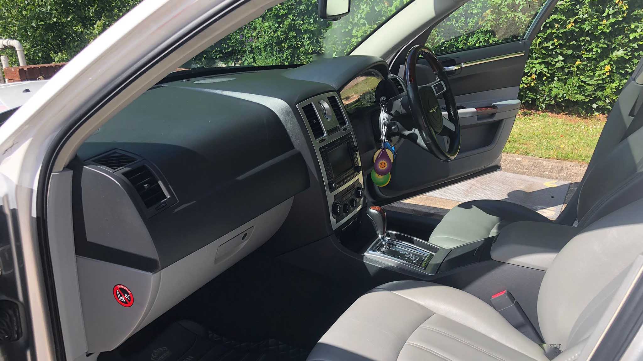 Front interior of white Chrysler 300C wedding car, showing grey leather seats, dashboard and chrome trim.
