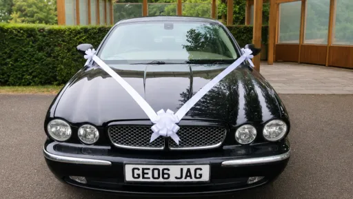 Front view of black Jaguar stretch limousine decorated with white wedding ribbons.