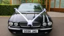 Front view of black Jaguar stretch limousine decorated with white wedding ribbons.