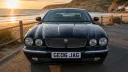 Front angle view of black Jaguar limousine parked beside coastline at sunset.