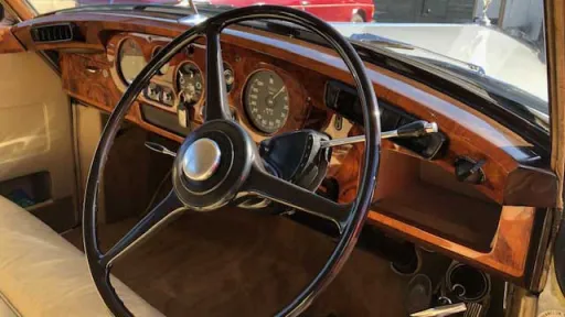 Close-up of polished wooden dashboard and vintage steering wheel inside Rolls-Royce Silver Cloud.