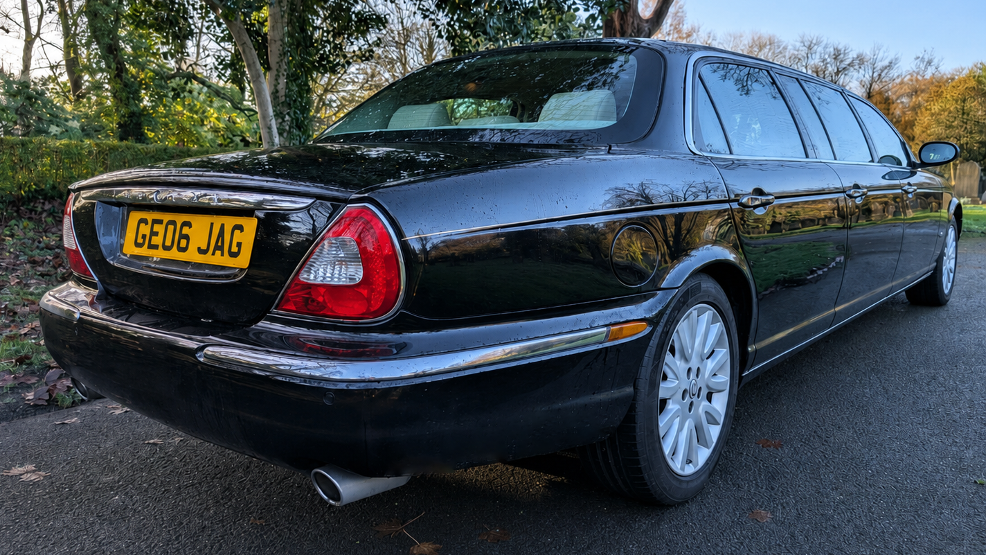 Rear side view of black Jaguar stretch limousine with extended body and chrome detailing.