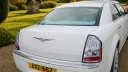 Rear view of white Chrysler 300C wedding car showing chrome bumper, tail lights and alloy wheels, parked on a gravel driveway.