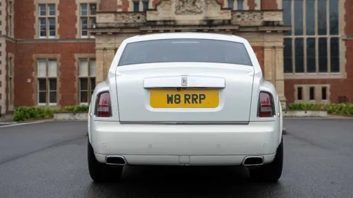 Rear view of white Rolls-Royce Phantom Series II EWB parked outside luxury venue.