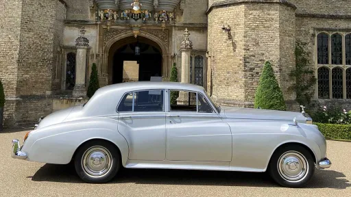 Side profile of silver Rolls-Royce Silver Cloud parked outside historic stone wedding venue.