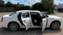Side view of white Chrysler 300C wedding car with front and rear doors open, showing grey leather interior and gold ribbons tied to the door handles.