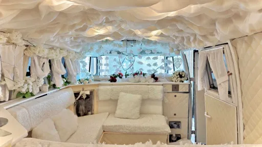 Luxury interior of ivory and sage green Volkswagen Split Screen campervan decorated for weddings with cream seating and floral drapes.