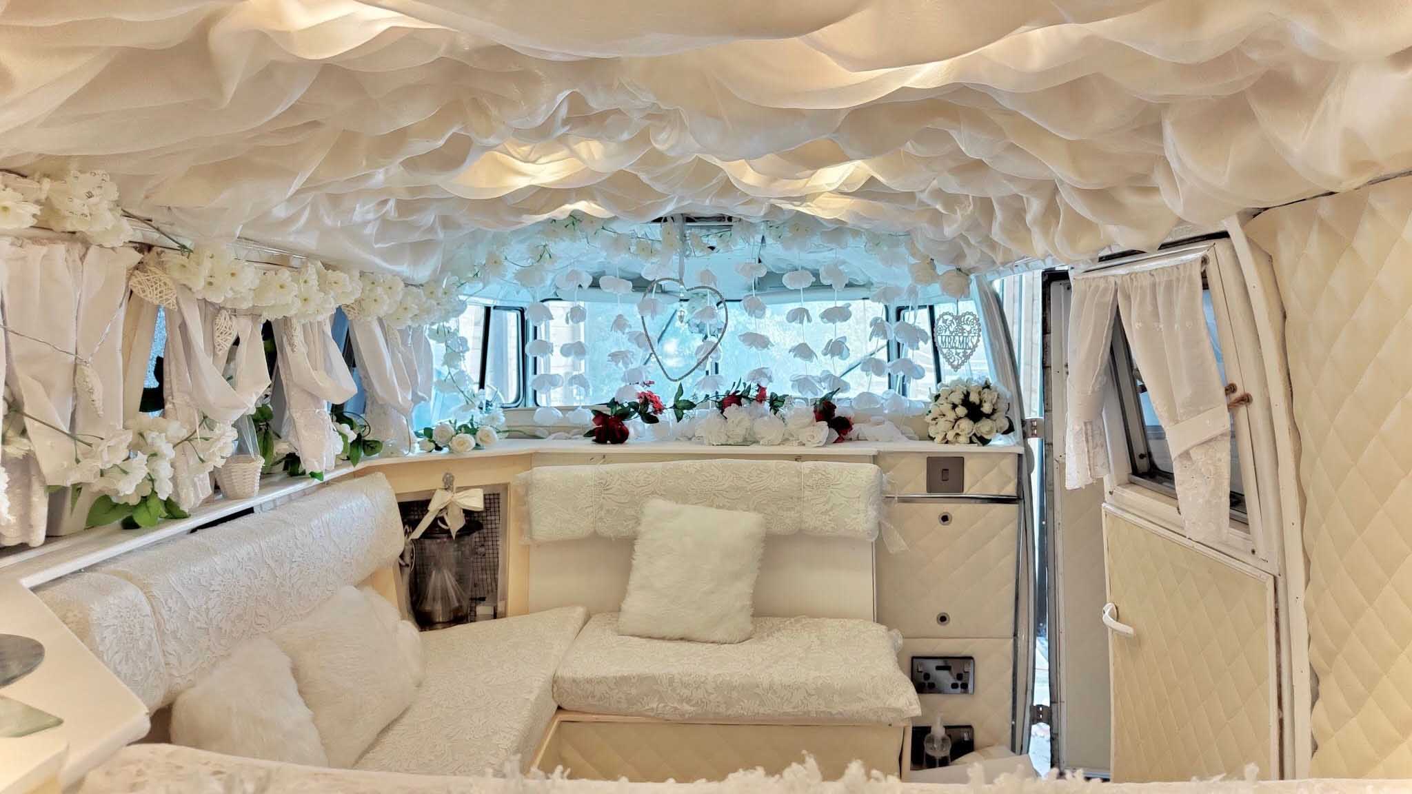 Luxury interior of ivory and sage green Volkswagen Split Screen campervan decorated for weddings with cream seating and floral drapes.