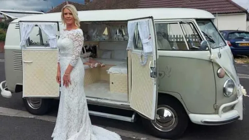 Bride standing beside ivory and sage green Volkswagen Split Screen campervan with side doors open in Devon.