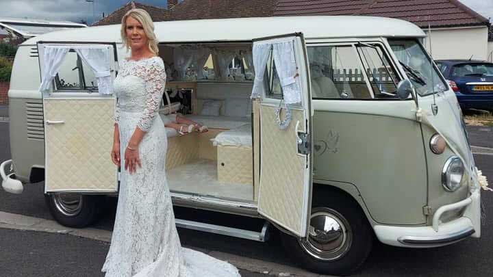 Bride standing beside ivory and sage green Volkswagen Split Screen campervan with side doors open in Devon.
