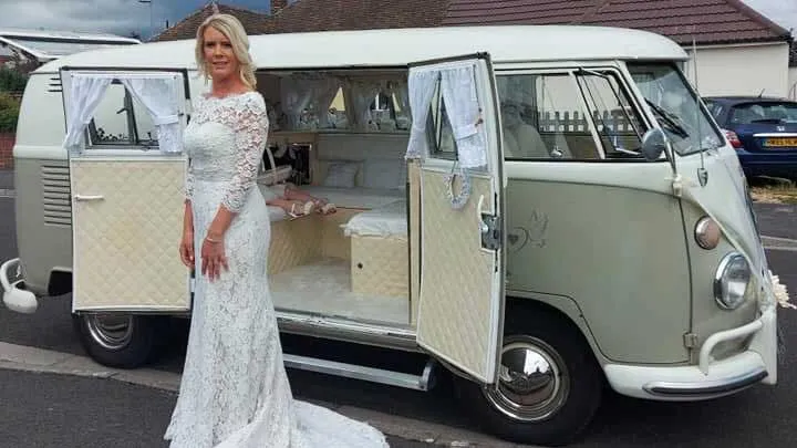 Bride standing beside ivory and sage green Volkswagen Split Screen campervan with side doors open in Devon.
