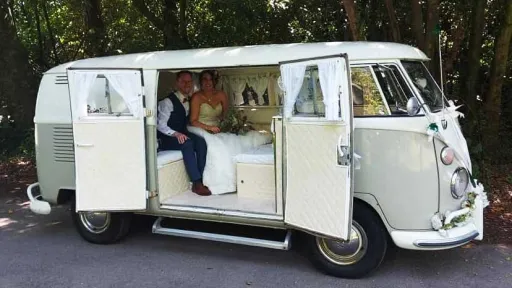 Wedding couple seated inside ivory and sage green Volkswagen Split Screen campervan in Devon.