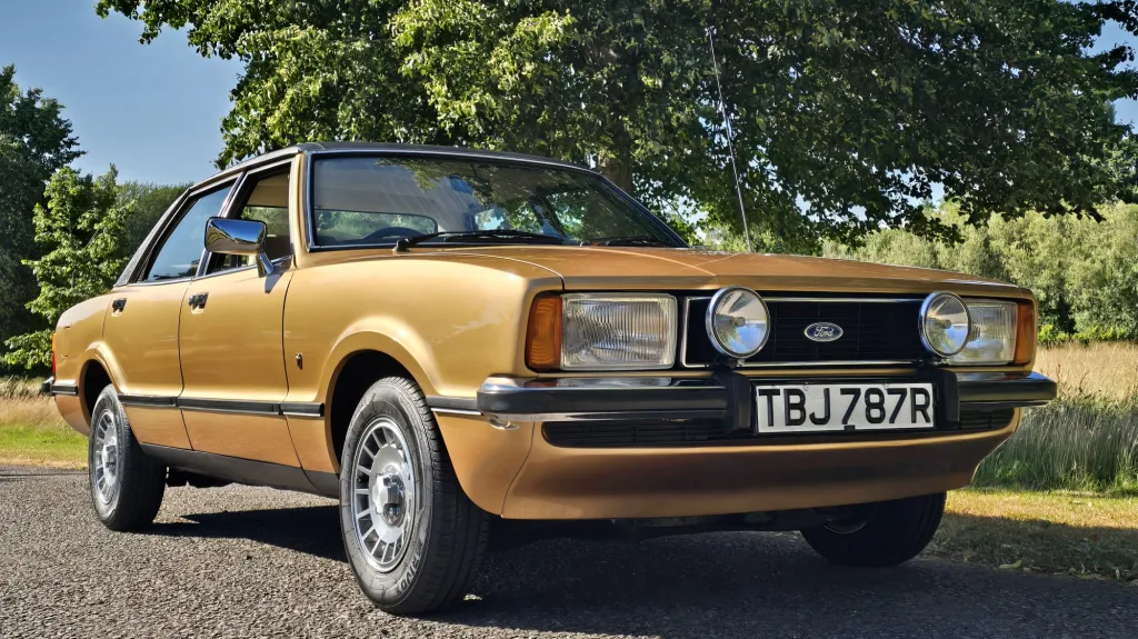 Gold Ford Cortina Mk4 Ghia wedding car parked beneath trees in Dorset countryside.