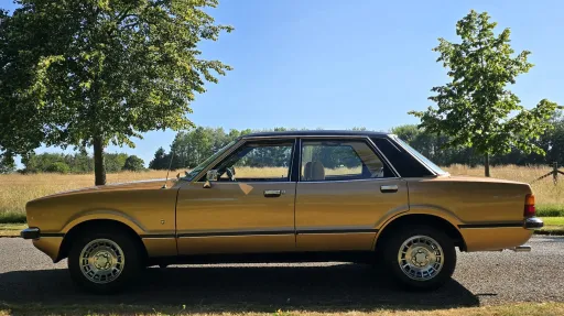 Full left side profile of gold Ford Cortina Mk4 Ghia parked in countryside location.