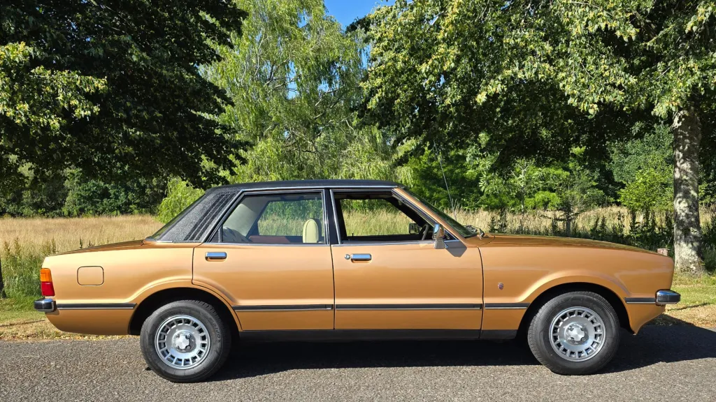 Full right side profile of gold Ford Cortina Mk4 Ghia parked on grass in rural setting.