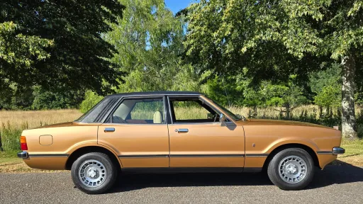 Full right side profile of gold Ford Cortina Mk4 Ghia parked on grass in rural setting.