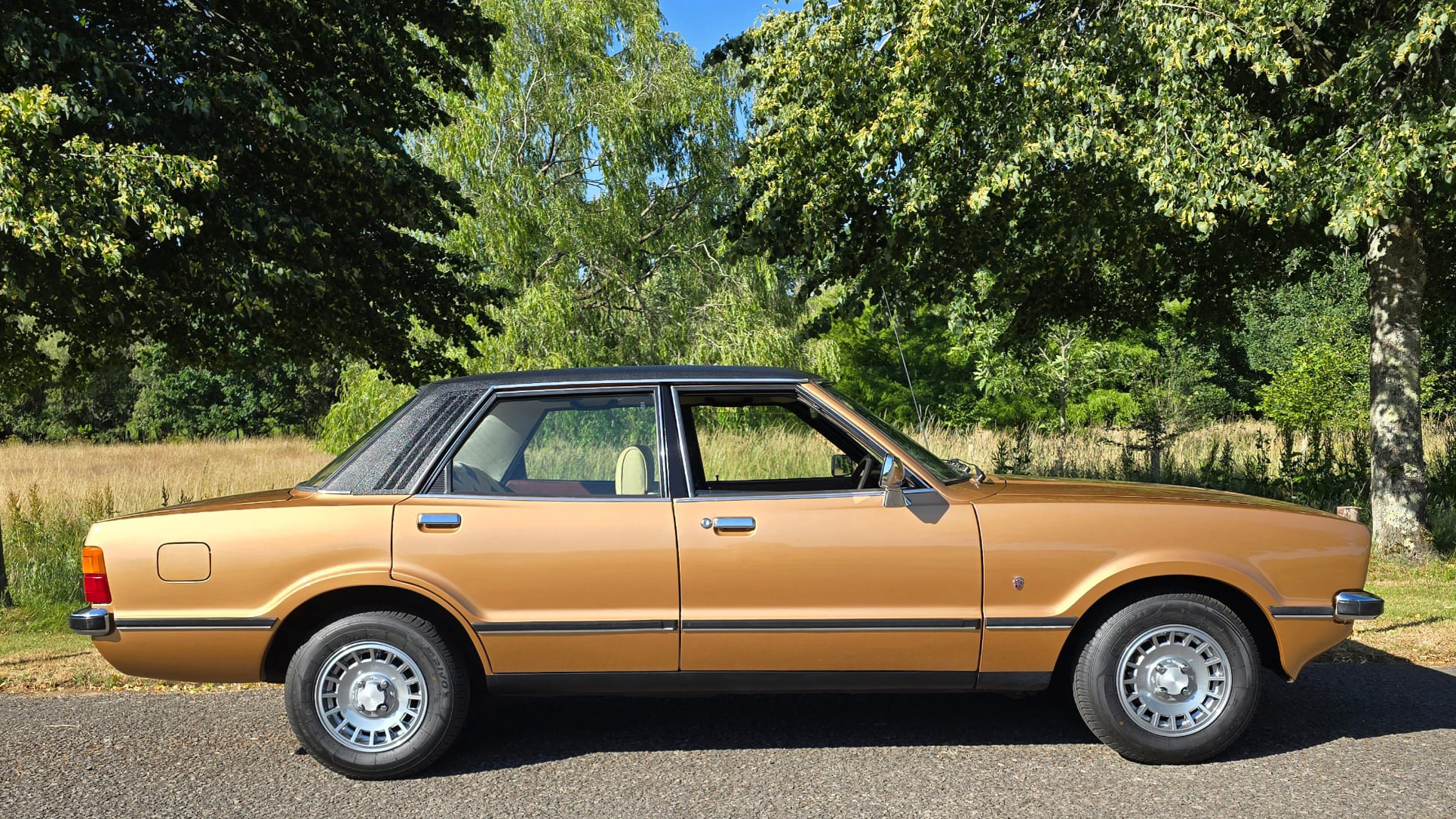 Full right side profile of gold Ford Cortina Mk4 Ghia parked on grass in rural setting.