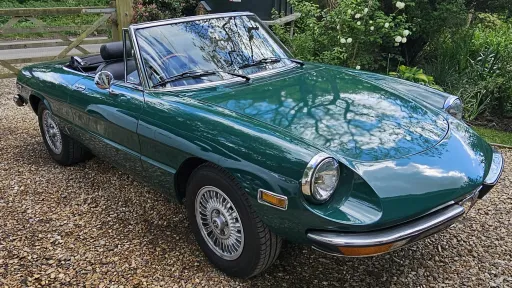 Green Alfa Romeo Spider Veloce 2000 convertible with soft top folded down in countryside setting.