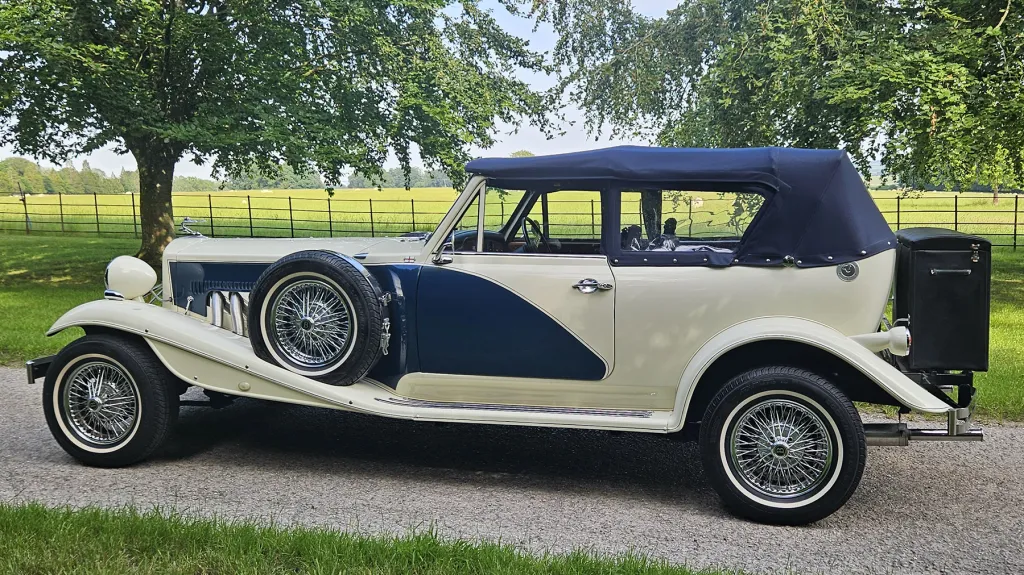 Blue and ivory Beauford wedding car with navy soft top roof parked on countryside driveway.
