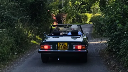 Rear view of green Alfa Romeo Spider Veloce 2000 convertible driving along country lane with roof down.