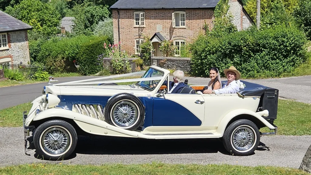 Blue and ivory Beauford convertible with roof folded down outside countryside wedding venue.