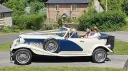 Blue and ivory Beauford convertible with roof folded down outside countryside wedding venue.