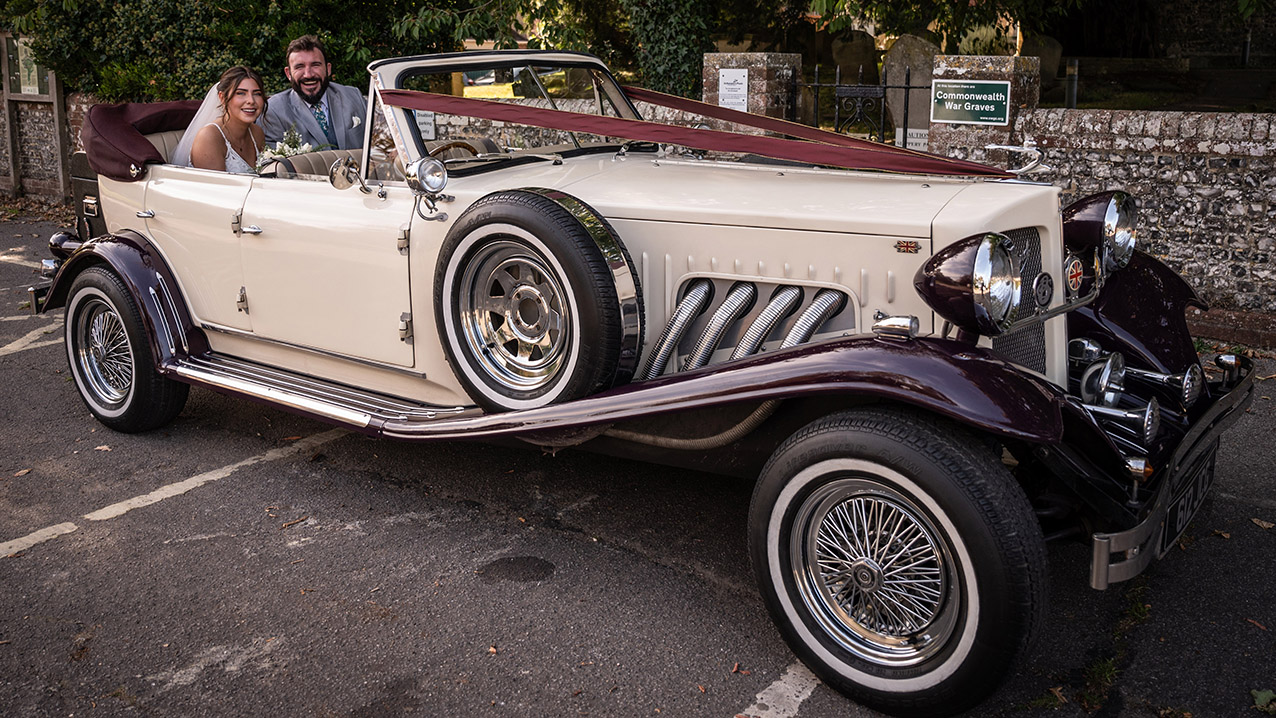 Front three quarter view of burgundy and cream Beauford convertible with burgundy soft top folded down and chrome wire wheels.