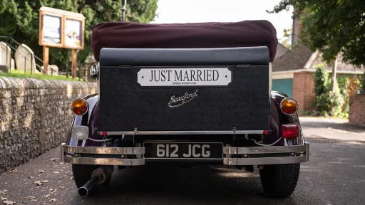 Rear view of burgundy and cream Beauford convertible with burgundy soft top raised and "Just Married" sign.
