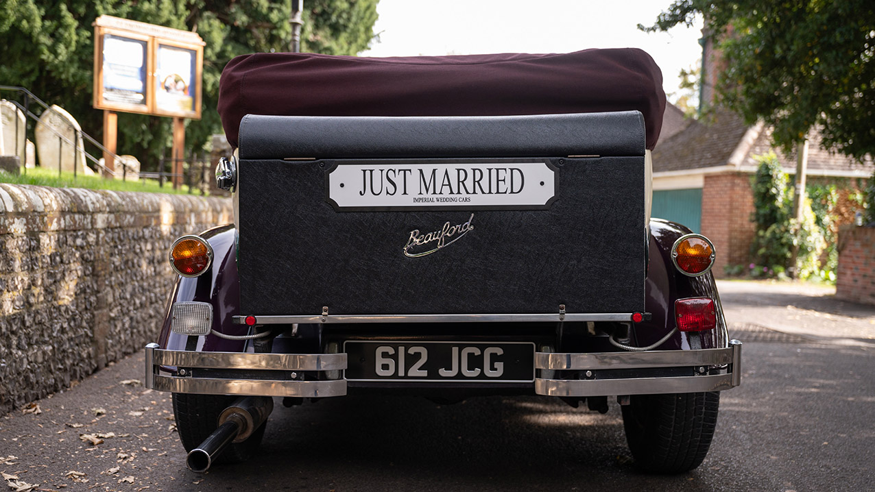 Rear view of burgundy and cream Beauford convertible with burgundy soft top raised and "Just Married" sign.