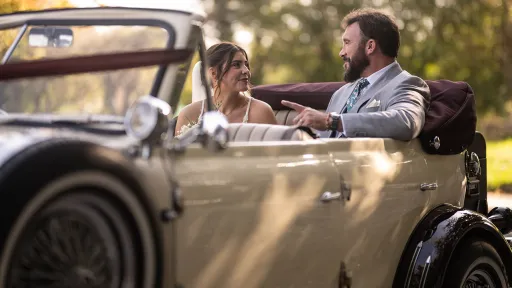 Bride and groom seated inside burgundy and cream Beauford convertible enjoying the open top journey.