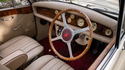 Classic wooden dashboard, cream leather seats and vintage steering wheel inside burgundy and cream Beauford convertible.