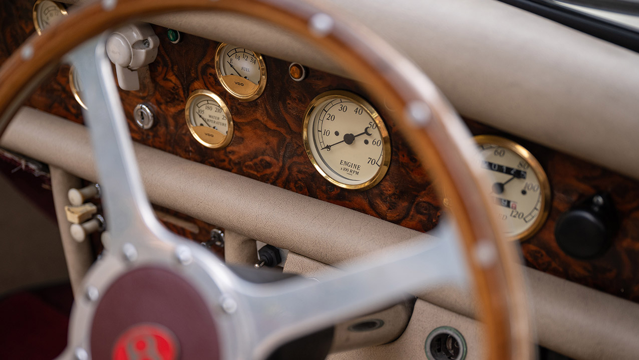 Close up of classic wooden dashboard and vintage instruments inside burgundy and cream Beauford wedding car.