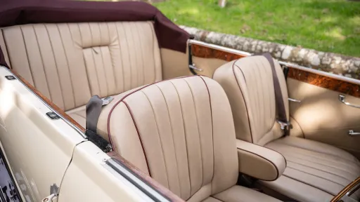 Cream leather rear seating inside burgundy and cream Beauford convertible with burgundy hood folded down.