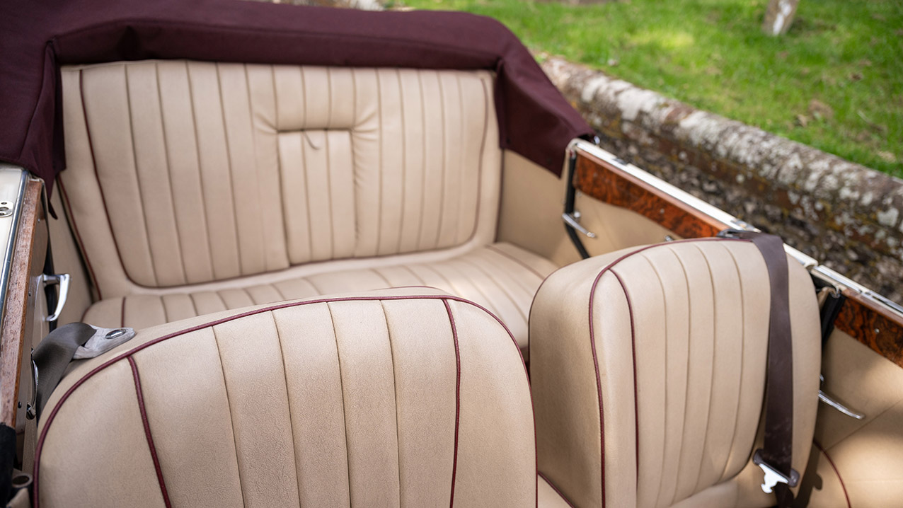 Cream leather front and rear seats inside four door Beauford convertible with burgundy trim and open roof.