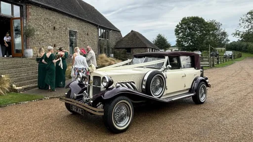 Burgundy and cream Beauford convertible with burgundy soft top roof raised outside country wedding venue.