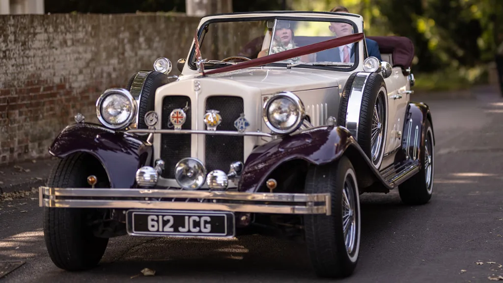 Front view of burgundy and cream Beauford convertible with chrome grille, spotlights and wedding ribbons in Salisbury.