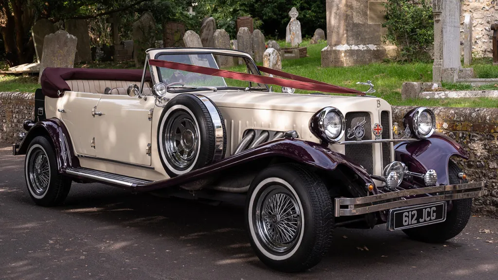 Front three quarter view of burgundy and cream Beauford convertible with chrome detailing and folded soft top.