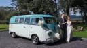 Bride and groom standing beside turquoise and white 1967 Volkswagen Split Screen campervan at wedding venue.