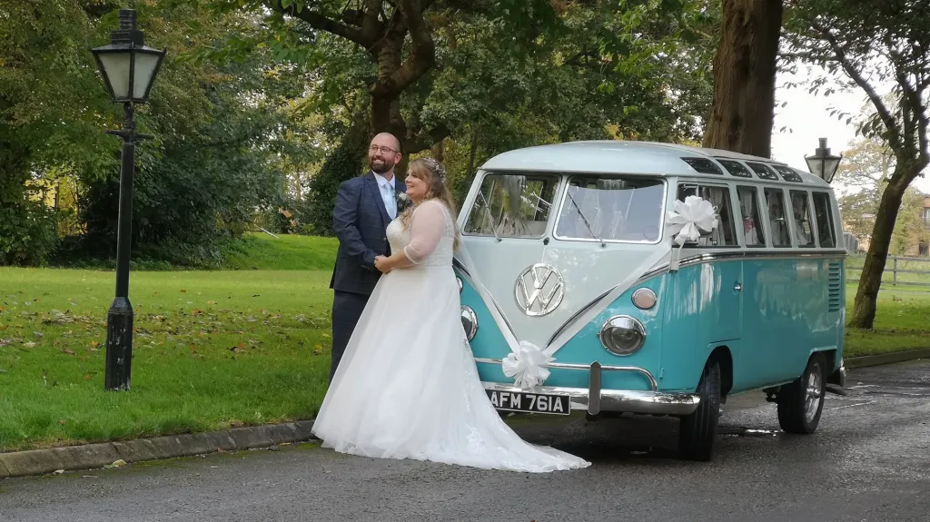 Bride and groom standing beside blue and white 1964 Volkswagen Split Screen Samba campervan.