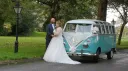 Bride and groom standing beside blue and white 1964 Volkswagen Split Screen Samba campervan.