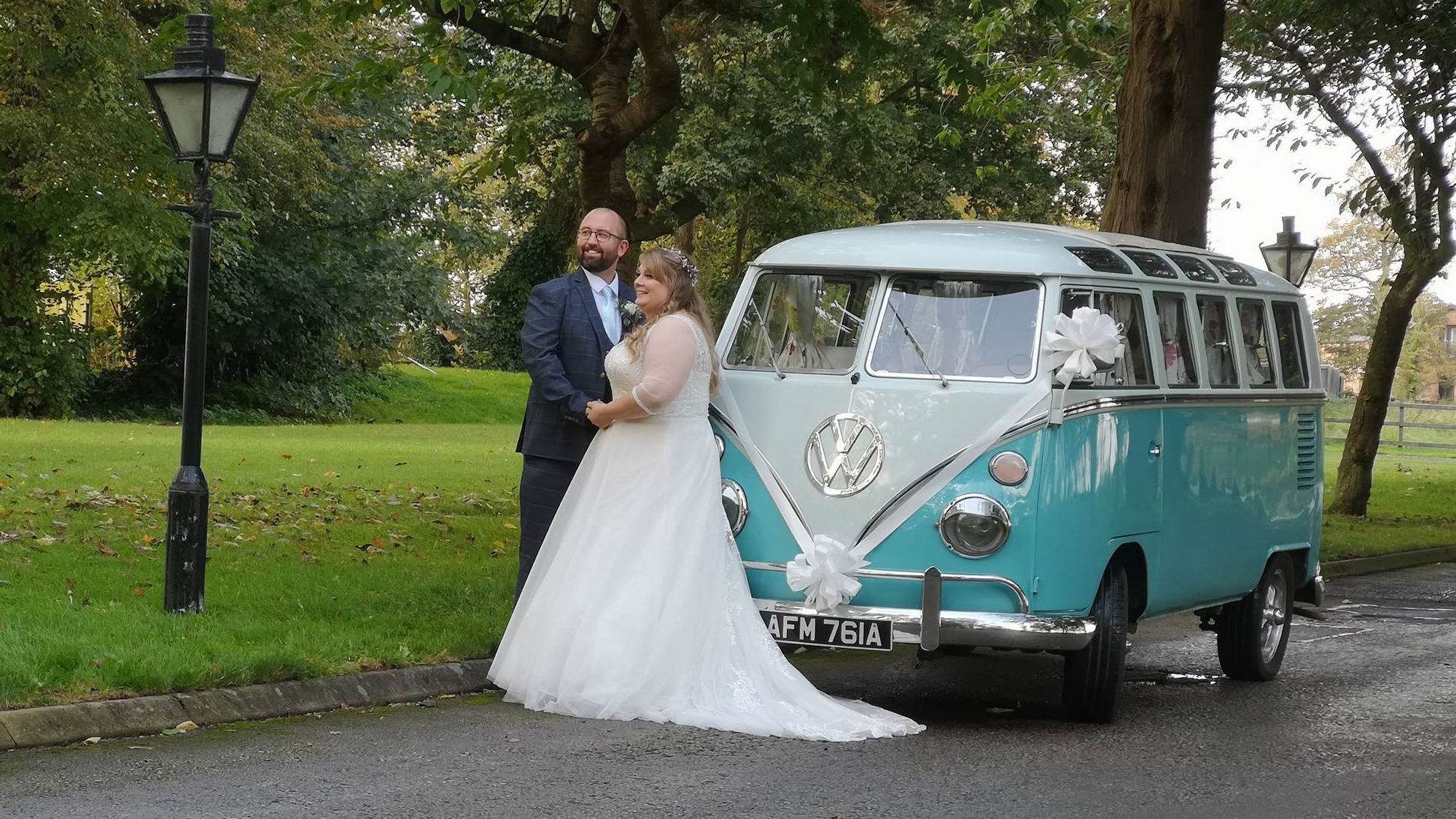 Bride and groom standing beside blue and white 1964 Volkswagen Split Screen Samba campervan.