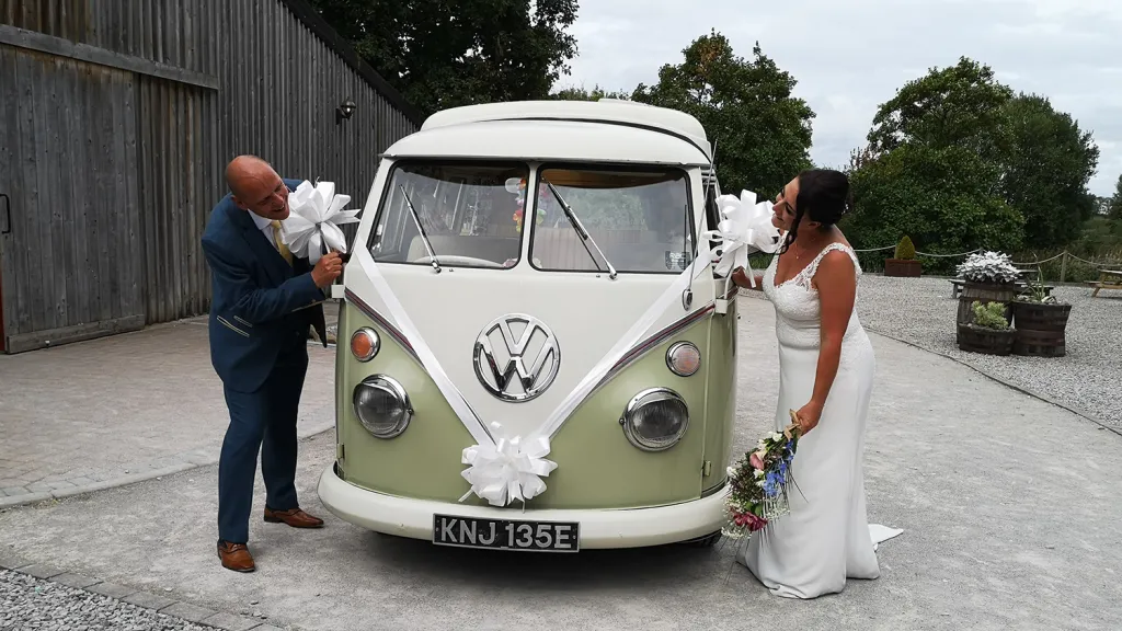 Bride and groom beside cream and green Volkswagen Split Screen campervan decorated for their wedding.