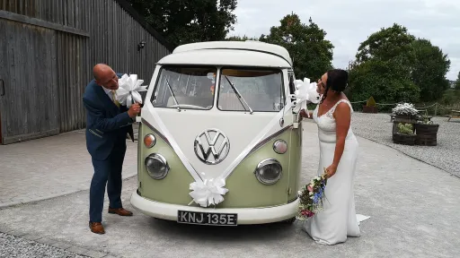 Bride and groom beside cream and green Volkswagen Split Screen campervan decorated for their wedding.