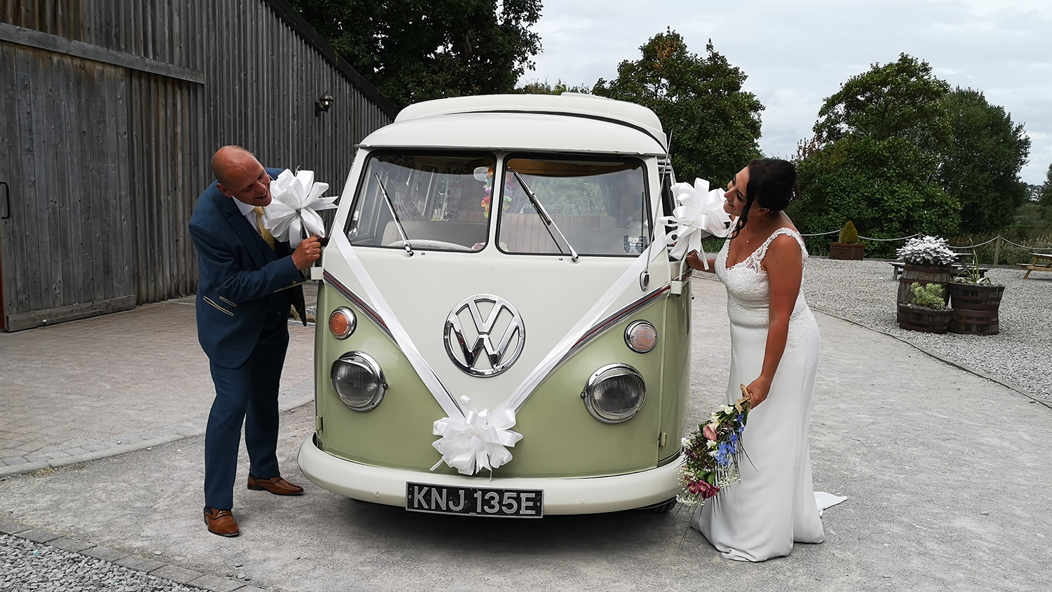 Bride and groom beside cream and green Volkswagen Split Screen campervan decorated for their wedding.