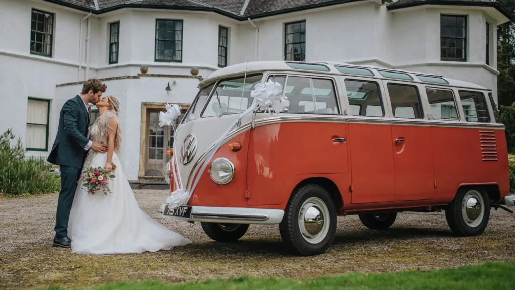 Bride and groom kissing in front of red and white 1962 Volkswagen Split Screen Microbus.